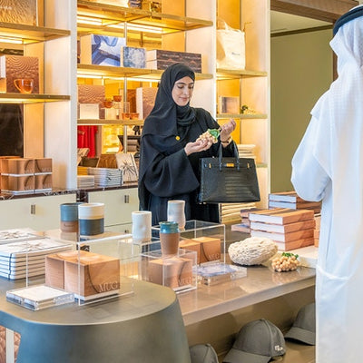 Woman in a store holding a black handbag, with a customer in the foreground.