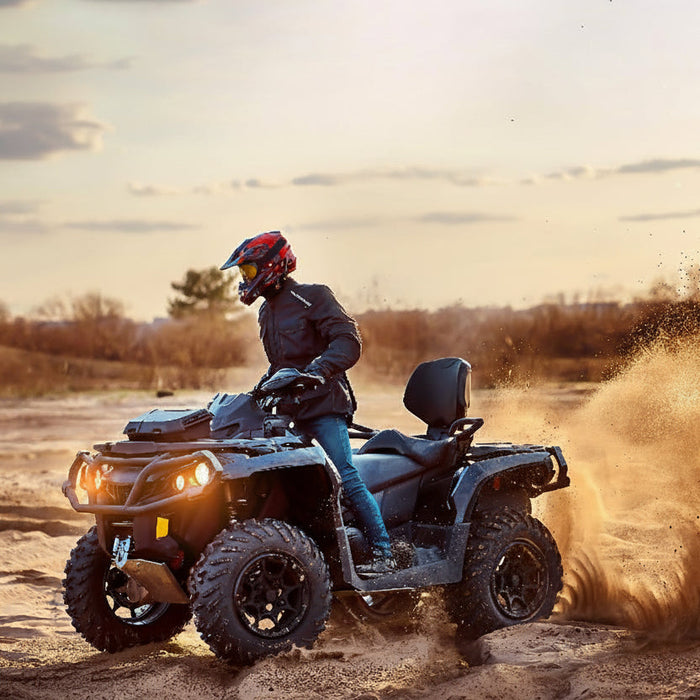 Person riding an ATV through a dirt field with a sunset in the background