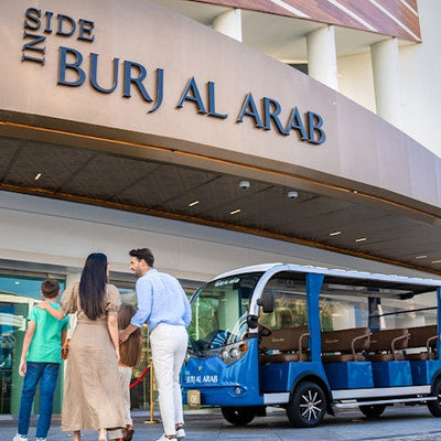 Family standing in front of a blue electric vehicle with 'Burj Al Arab' branding.