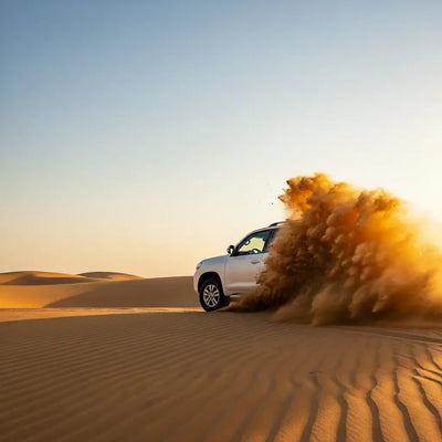 White SUV driving on sand dunes with dust in the air